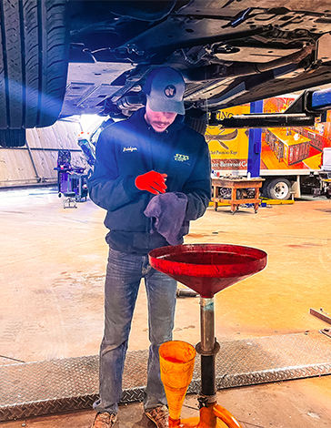 Fry's technician draining oil during a service, standing beneath a lifted vehicle